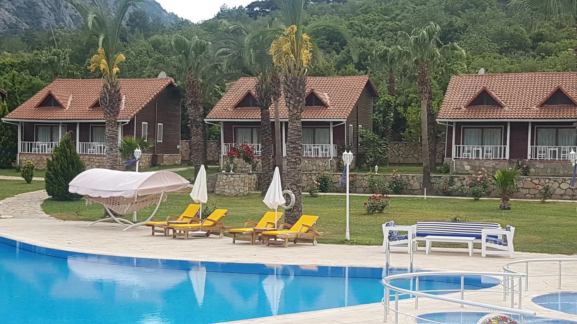 Club Sun Village havuz kenarında sıra ahşap bungalovlar ve Beydağları